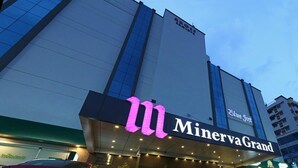 Entrada de un hotel con un llamativo letrero 'MinervaGrand', diseño arquitectónico moderno y un área de acceso visible con plantas en macetas.
