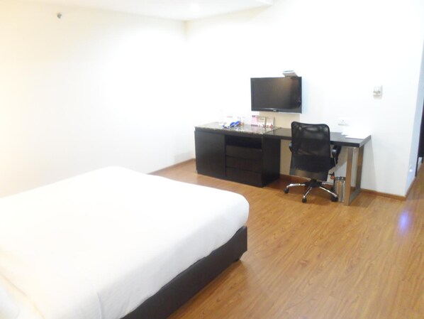 A hotel room with a bed, a desk, a chair, and a television.