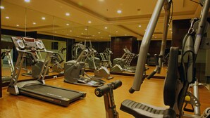 Un gimnasio con diversos equipos de ejercicio, incluyendo cintas de correr y máquinas de pesas, dispuesto en un espacio amplio con espejos en las paredes.