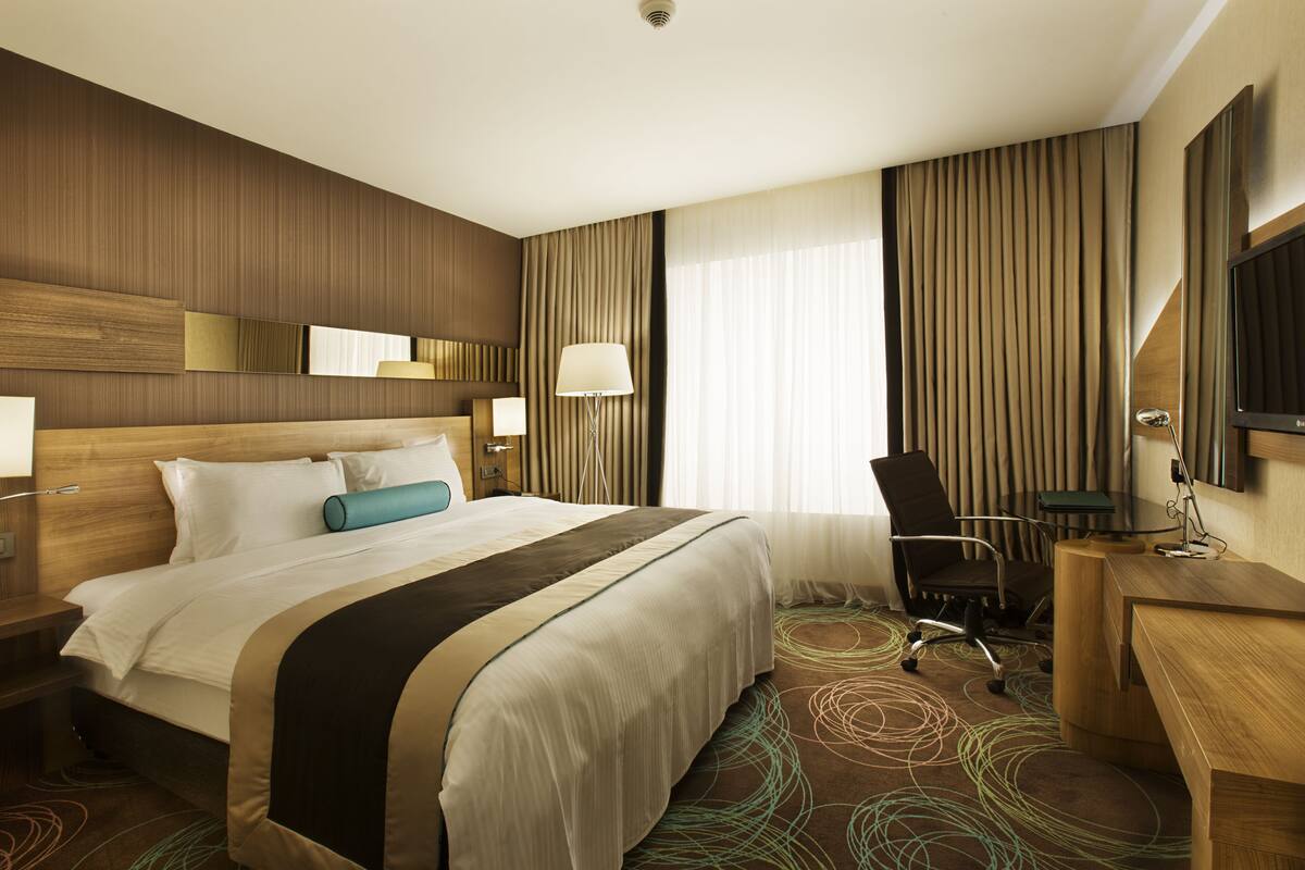 A hotel room with a large bed, a desk, a chair, and a TV.