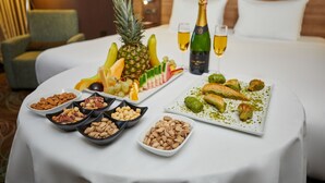 Un desayuno tipo buffet ordenado sobre una cama de hotel, con diversas frutas, nueces y bollería.