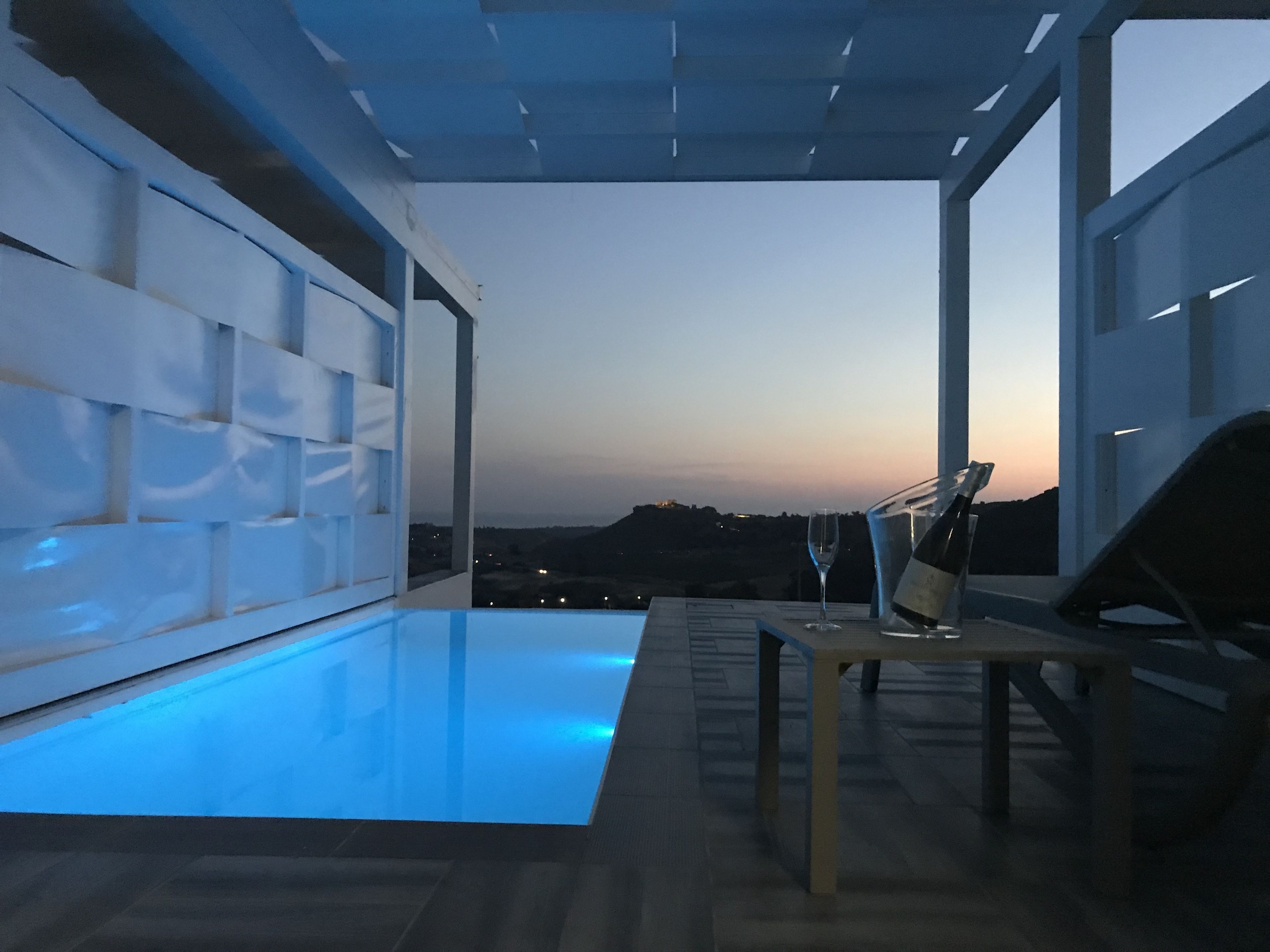 A modern indoor pool area with a clear view of the sunset and distant landscape.