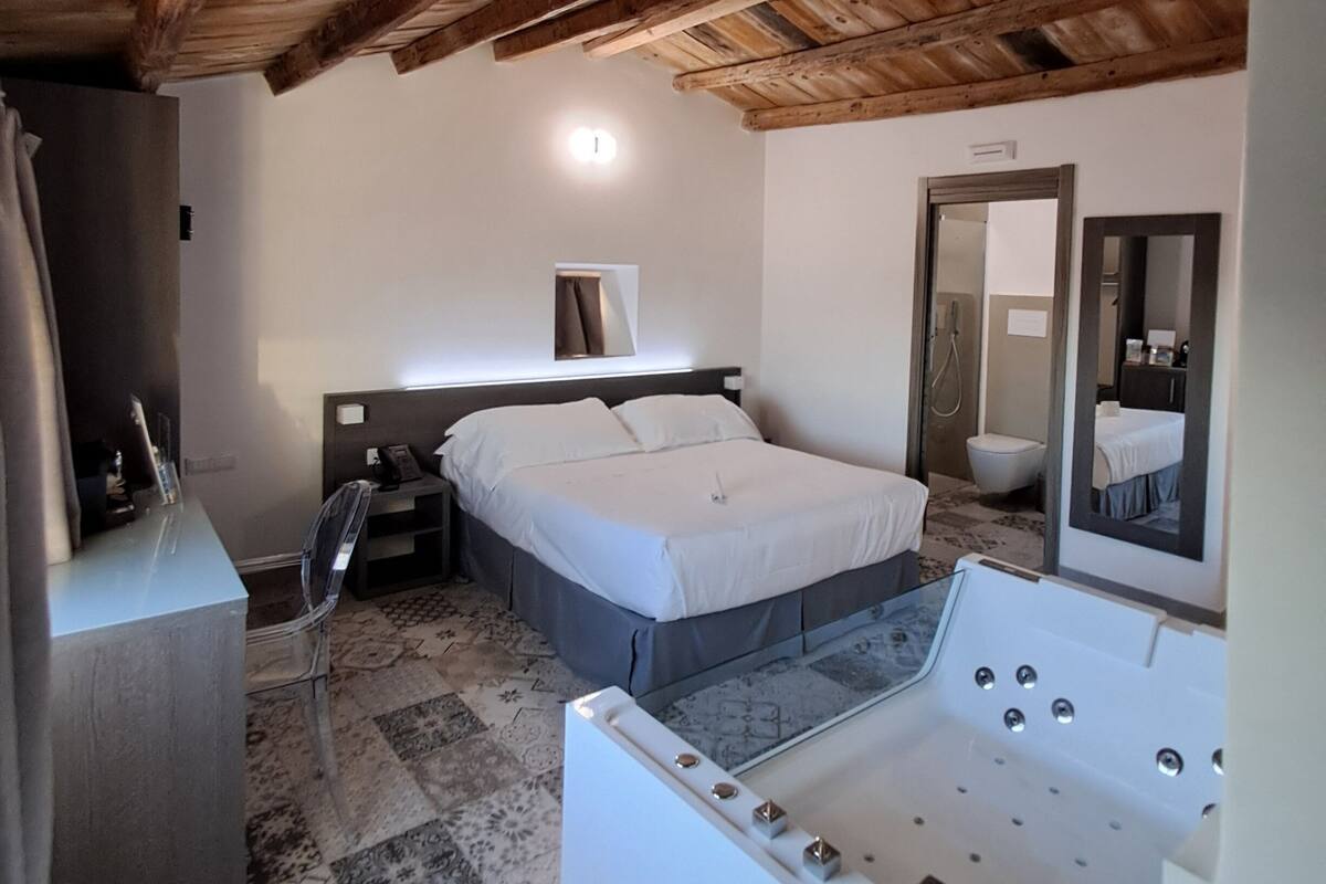 Un dormitorio con techo de madera, una cama, un escritorio, una silla, un espejo y una bañera.