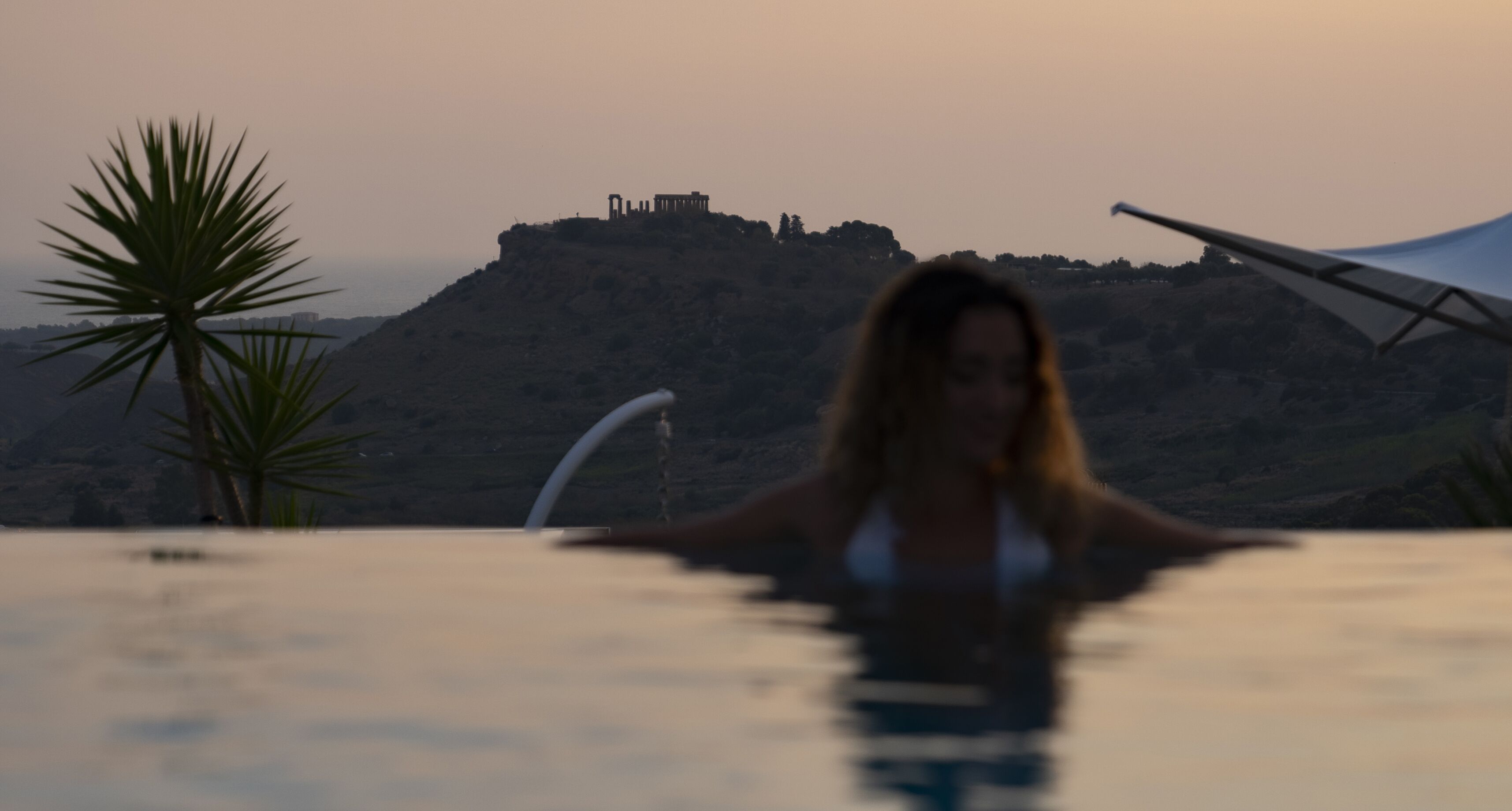 Eine Person in einem Schwimmbecken mit Blick auf einen Hügel und Ruinen im Hintergrund.
