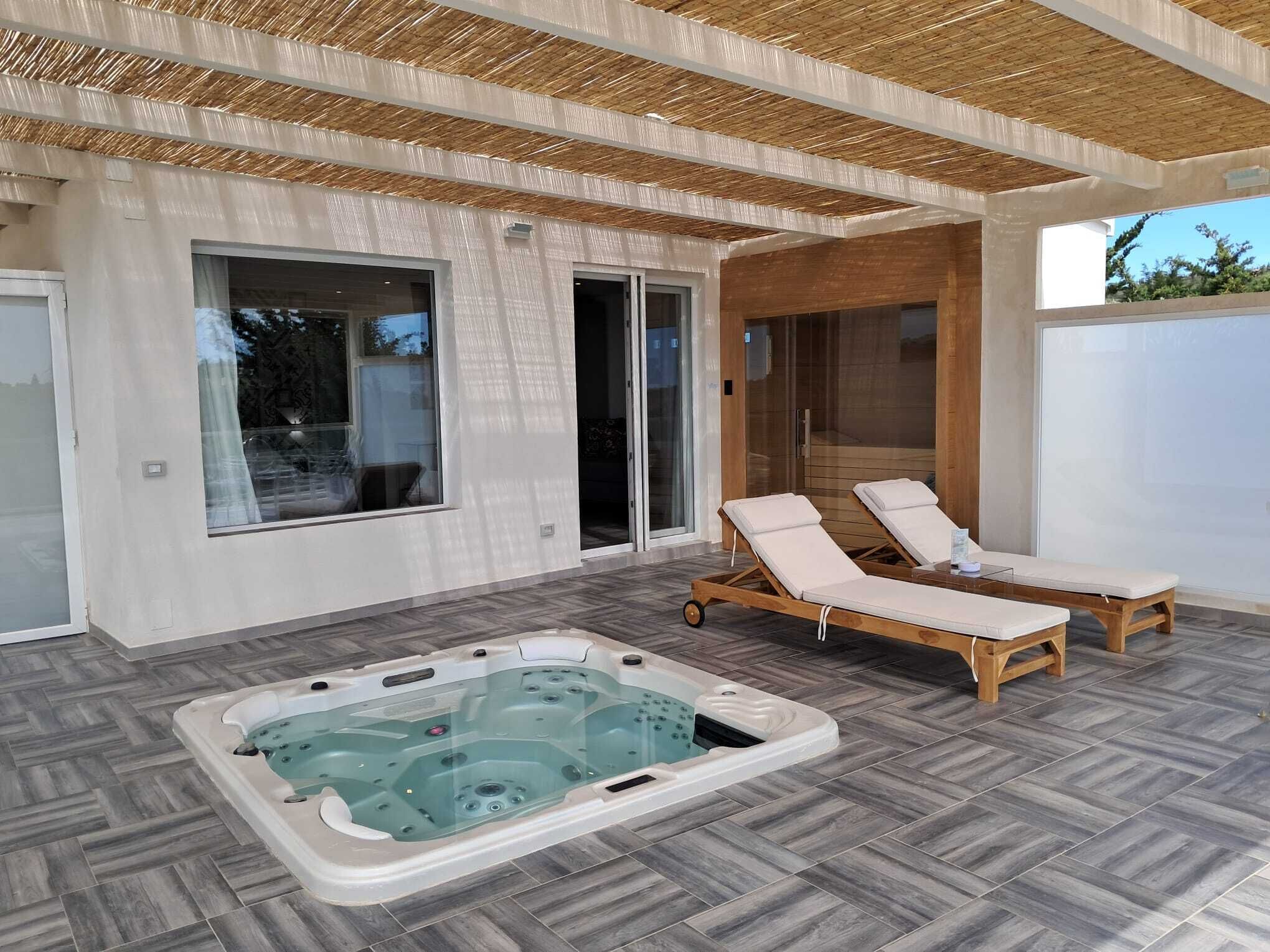 A modern outdoor area with a hot tub, lounge chairs, and a glass door leading to a covered patio.