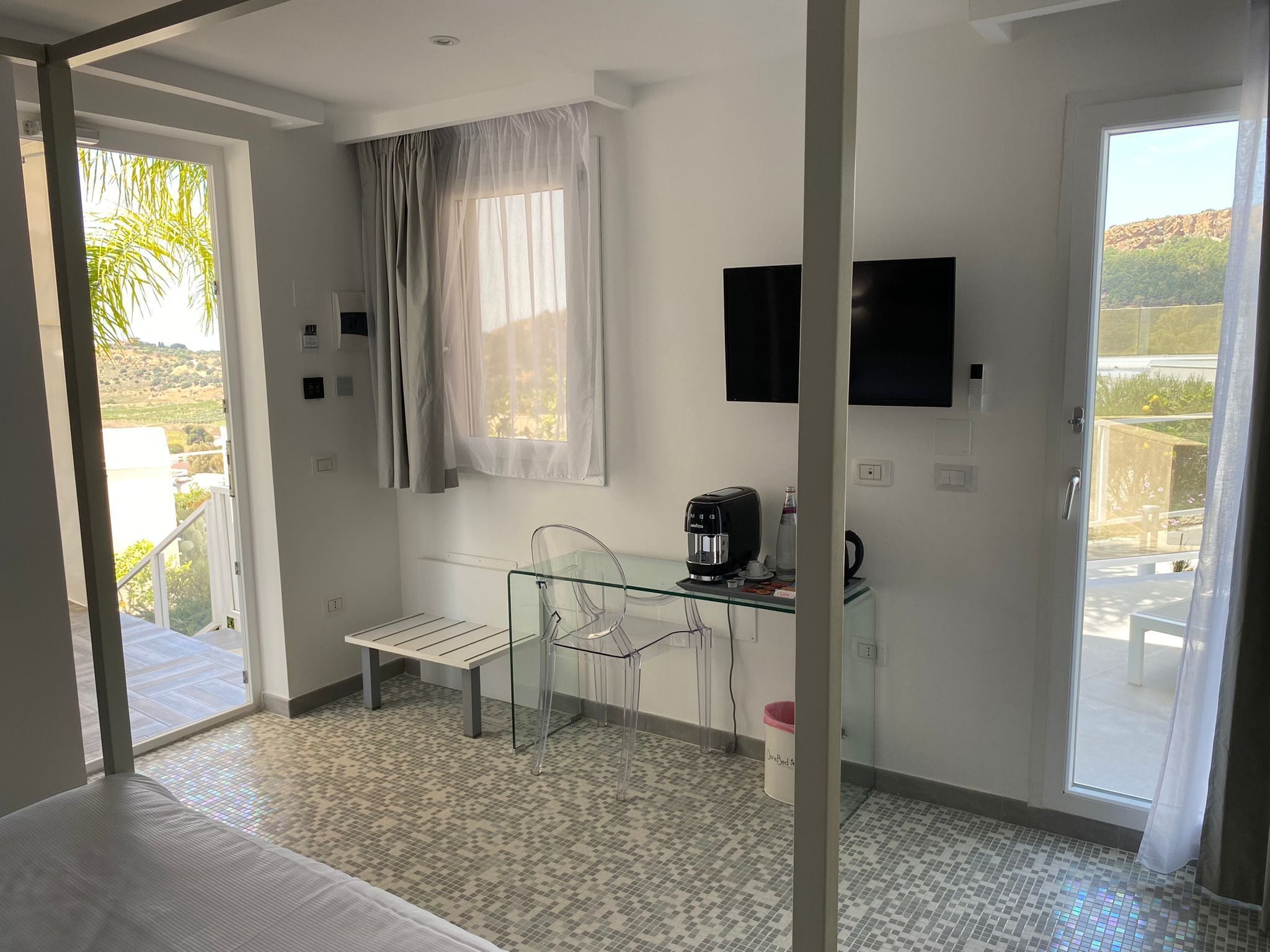 A hotel room with a bed, a desk with a chair, a coffee maker, and a TV on the wall.