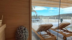 A wooden bench and a stone-filled basket in a room with large windows overlooking a terrace with lounge chairs. - Doric Eco Boutique Resort & Spa - Sicily (Agrigento)