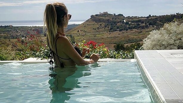 A person in a clear pool with a view of a hilly landscape and a castle in the distance. - Doric Eco Boutique Resort & Spa - Sicily (Agrigento)