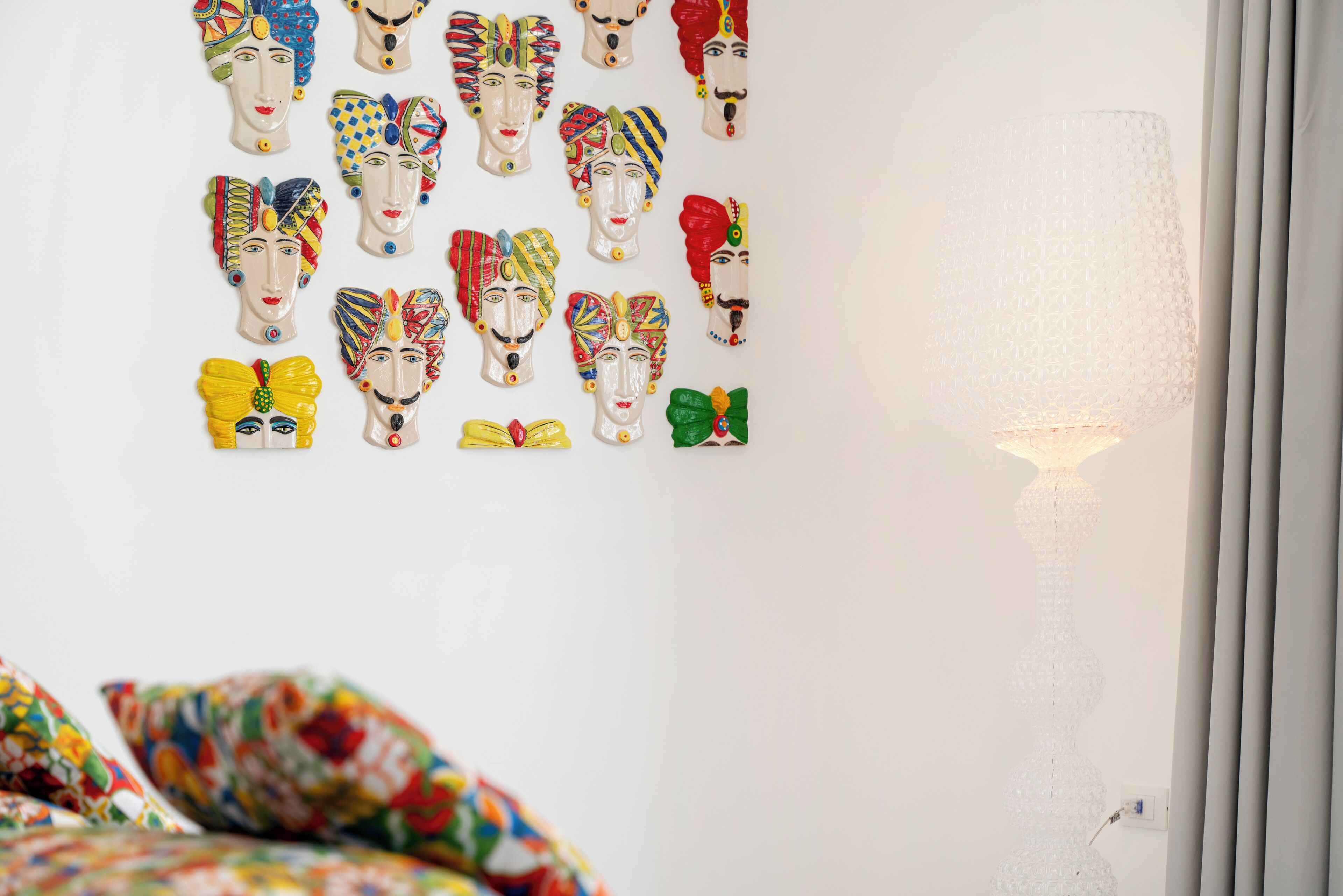 A wall with colorful masks and a floor lamp.