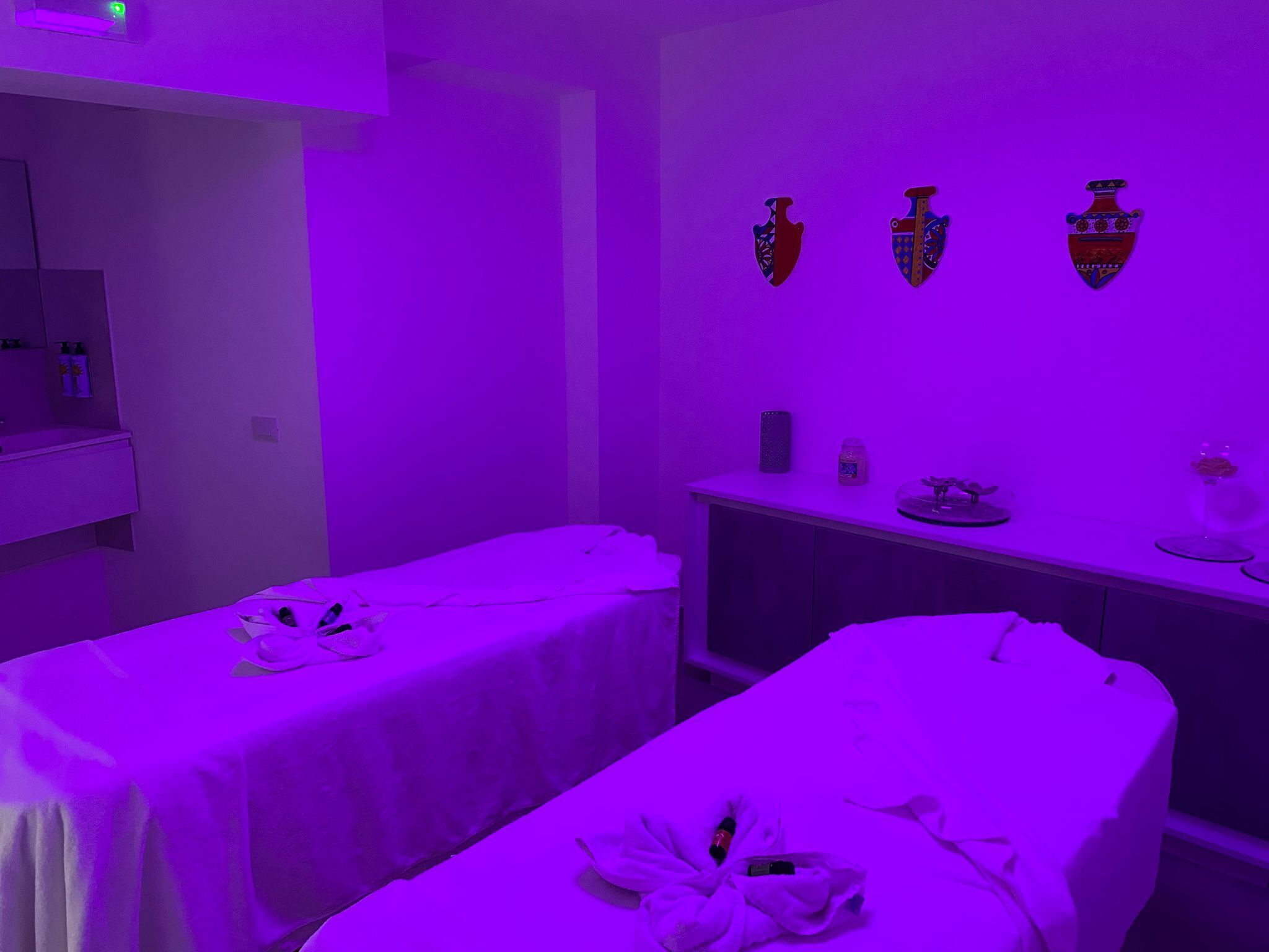 A room with two beds, a vanity with a mirror, and wall-mounted decorative vases.