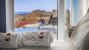 A hotel room with a bed, a window with a view of a hill and a castle, and two towels with the hotel name. - Doric Eco Boutique Resort & Spa - Sicily (Agrigento)