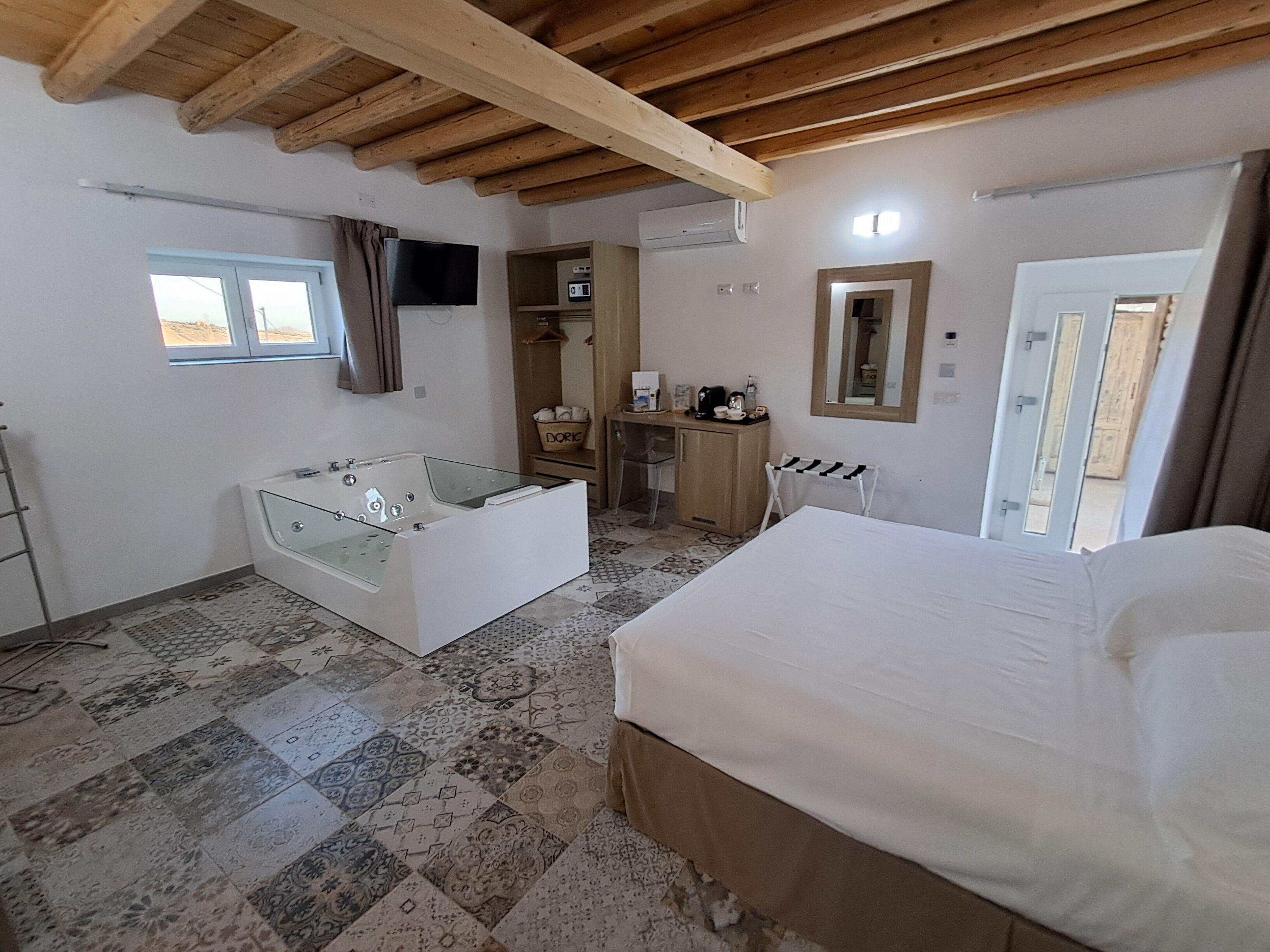 Camera da letto con un letto grande, una vasca da bagno vetrata, una scrivania, una sedia, un armadio e uno specchio.