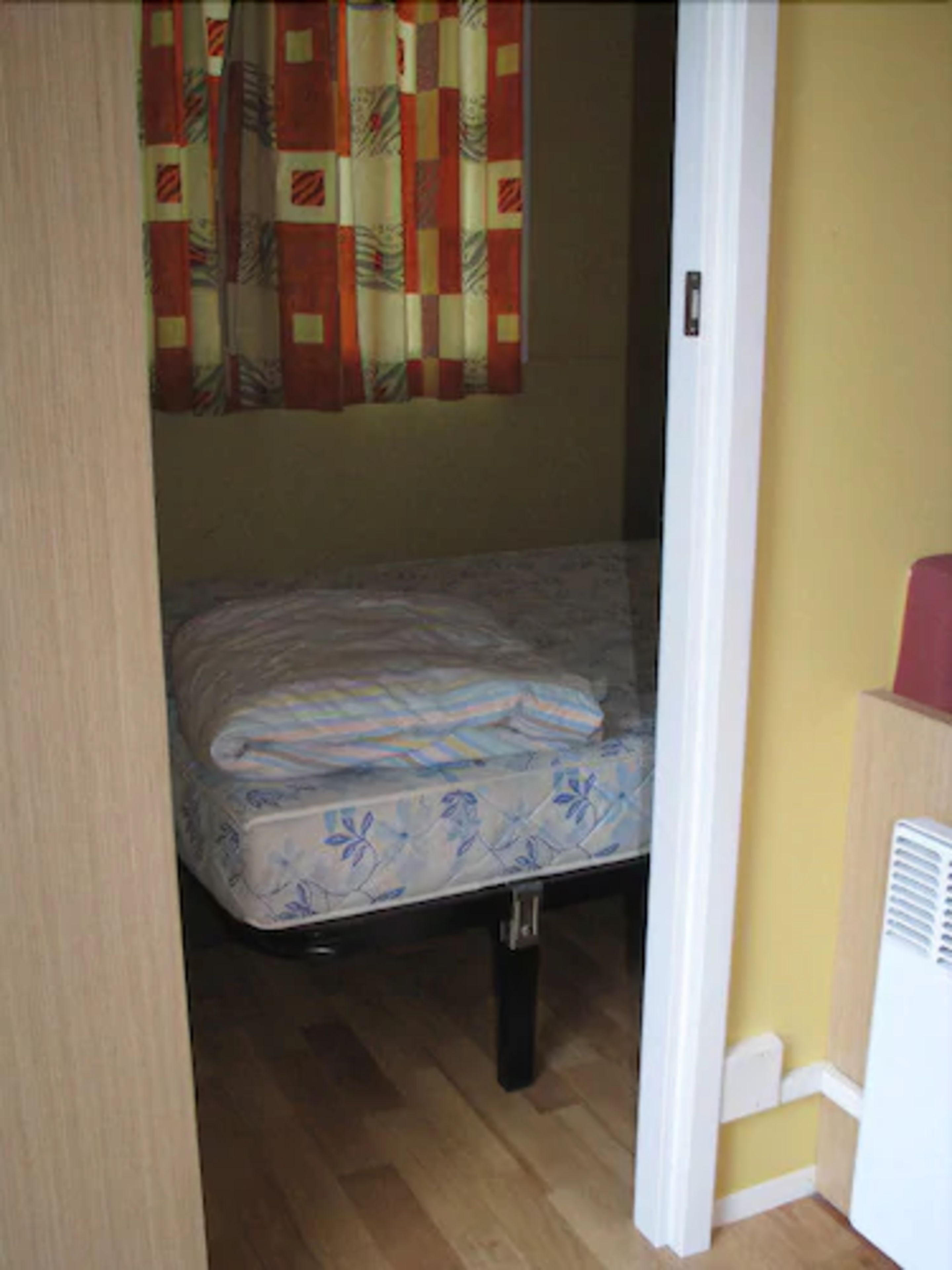 Una habitación pequeña y funcional con una cama individual, un calentador y una cortina.