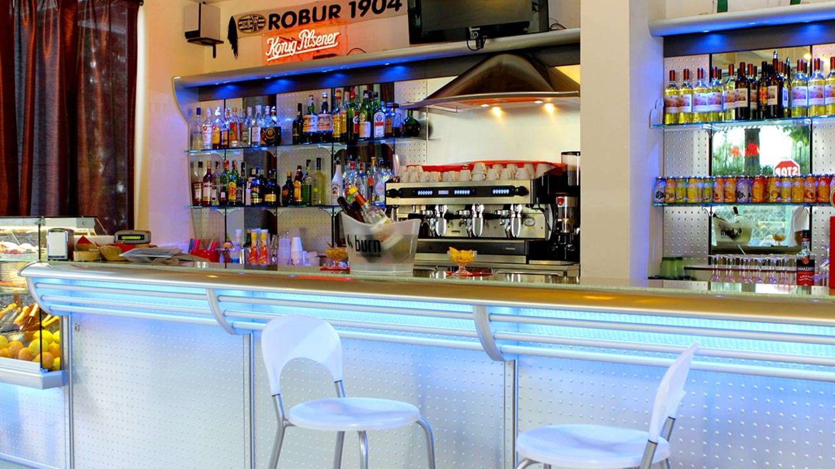 A bar area with a variety of liquor bottles, a coffee machine, and two white chairs.