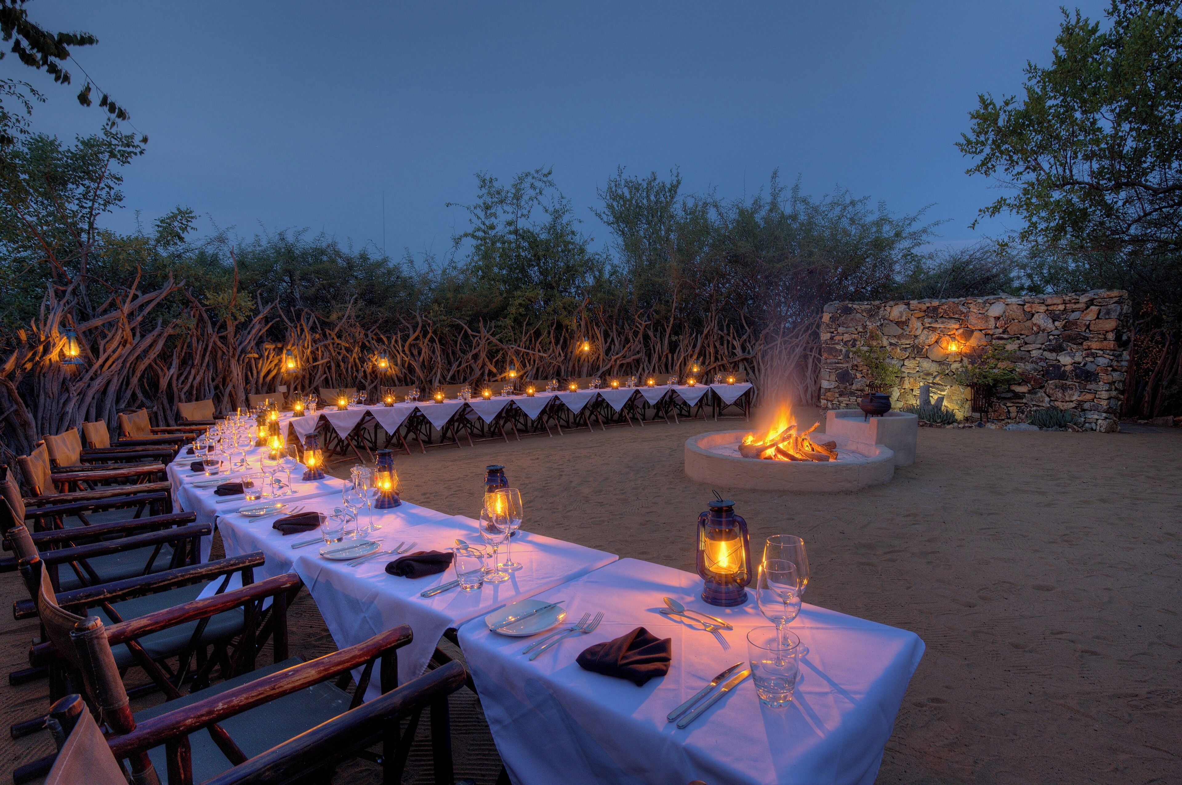 An outdoor dining area with tables set for a meal, surrounded by natural vegetation and stone walls.
