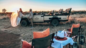 A safari vehicle with a table and chairs set up for an outdoor meal.