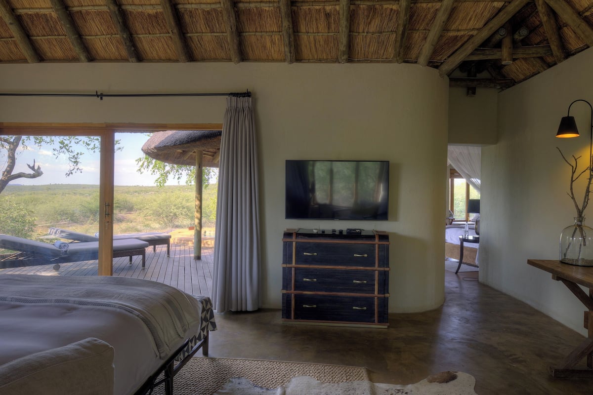 A bedroom with a large bed, a TV, a wooden dresser, and a view of the outdoors.