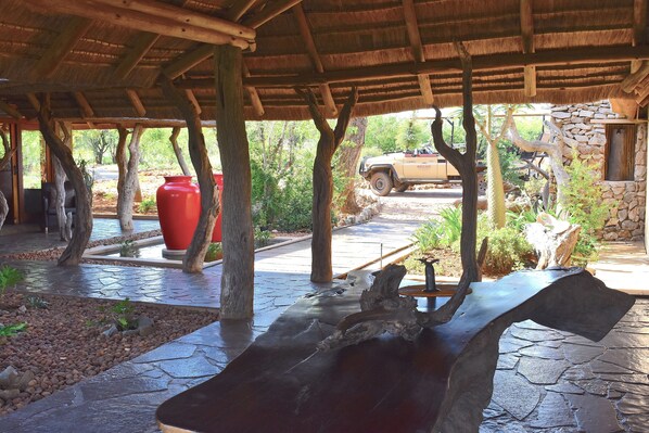 An outdoor covered area with a stone floor, wooden beams, and a large red pot.