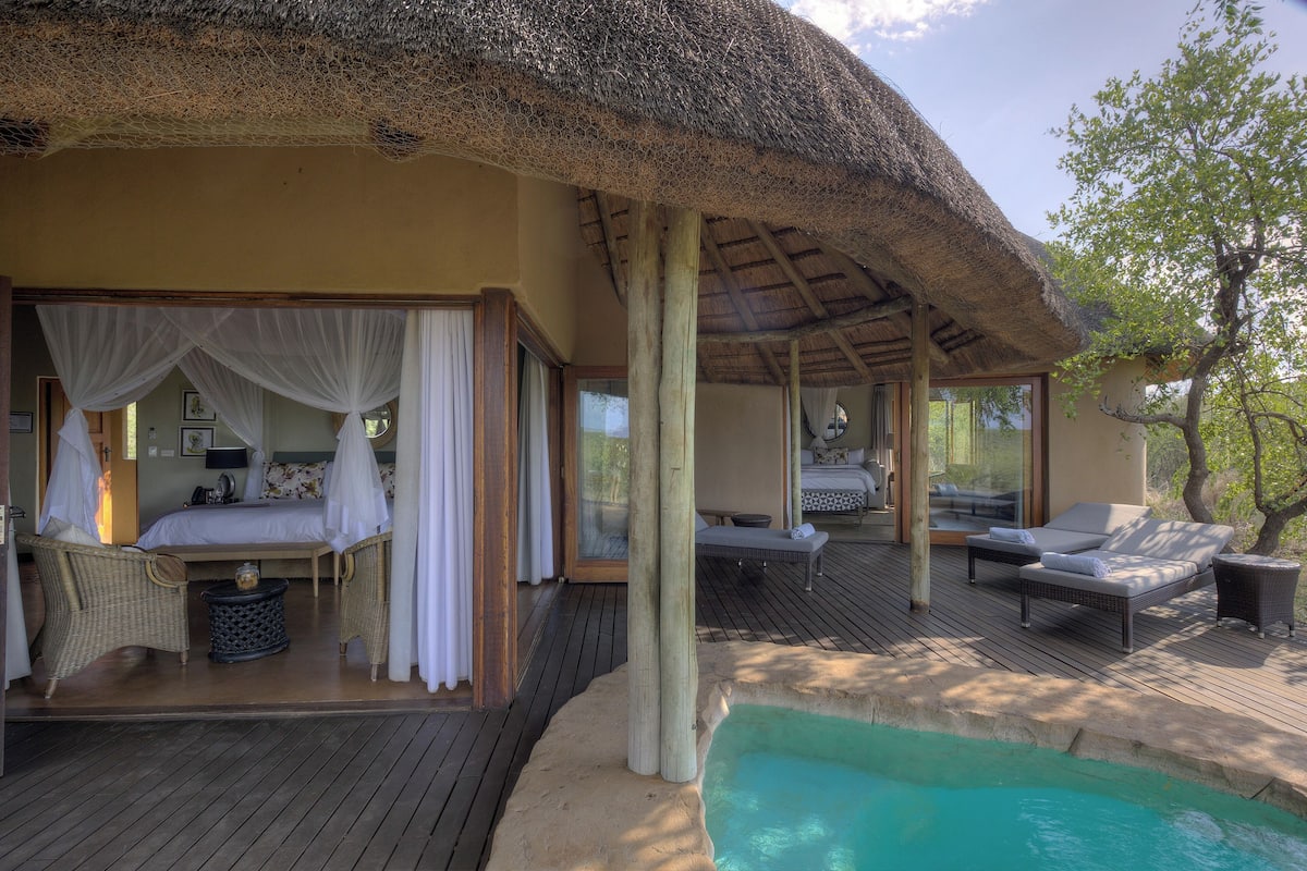 A thatched-roof bedroom with a bed, a small table, and a chair.