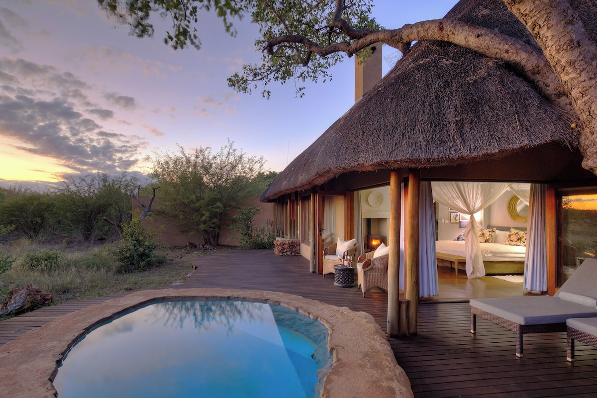 A thatched-roof building with a pool and outdoor seating area.