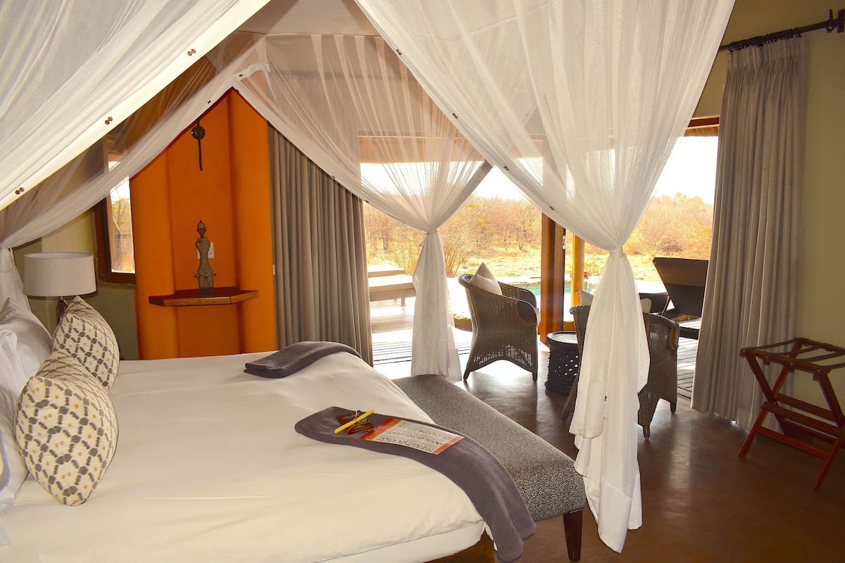 A bedroom with a bed, a bedside table, a chair, and a view of the outdoors.