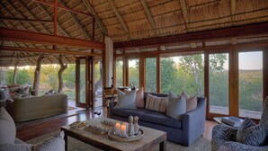 Amplia sala de estar con techo de paja, ventanas grandes que ofrecen vistas al exterior, un conjunto de sofás y una mesa de centro con objetos decorativos.