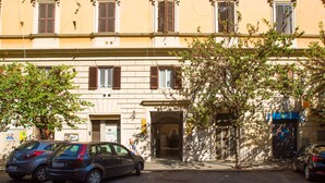 A building with a central entrance, multiple windows with shutters, and parked cars on the street. - Residenza Sistina (Rome)