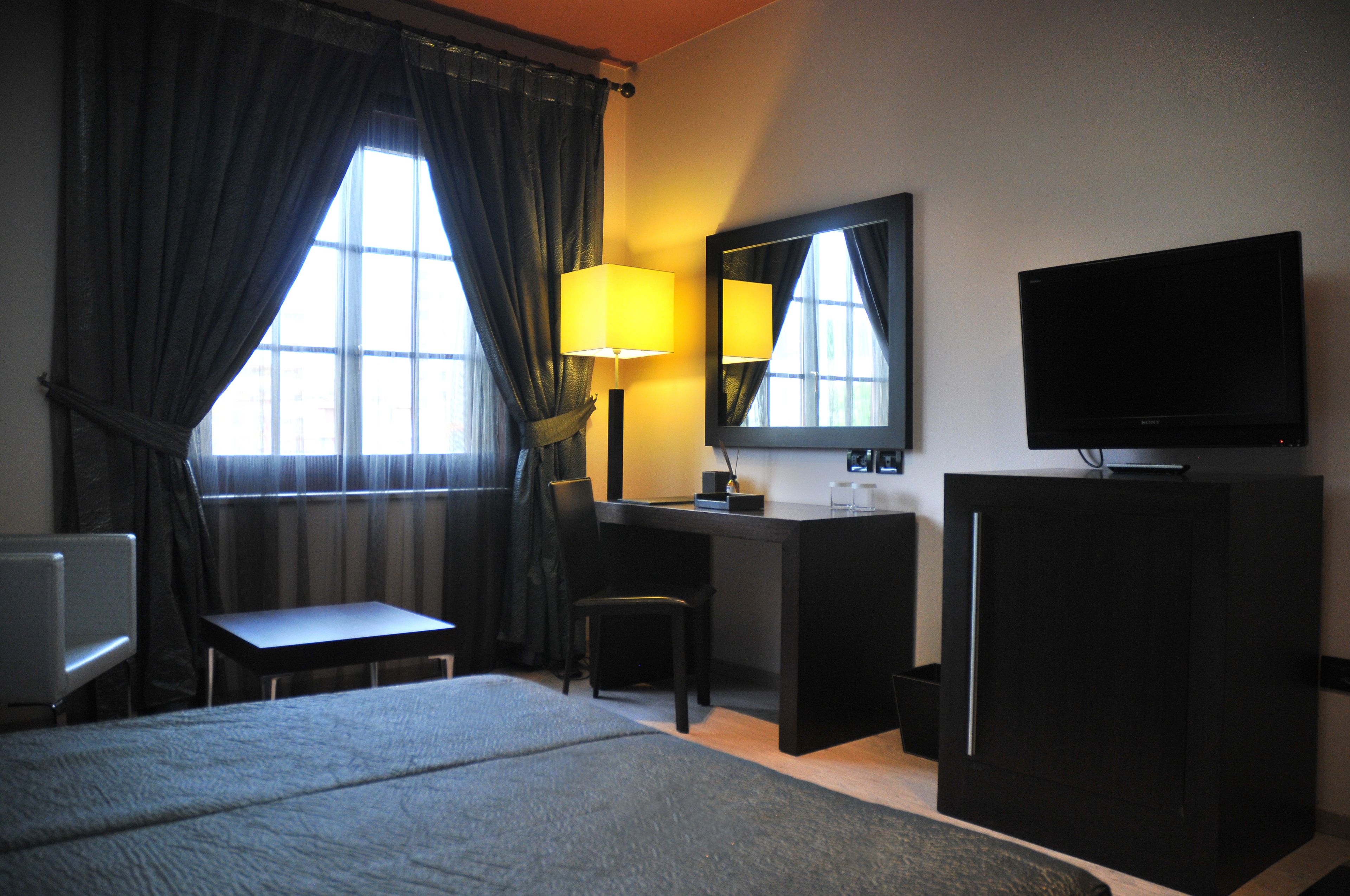 A hotel room with a bed, a desk, a chair, a television, and a window with curtains.