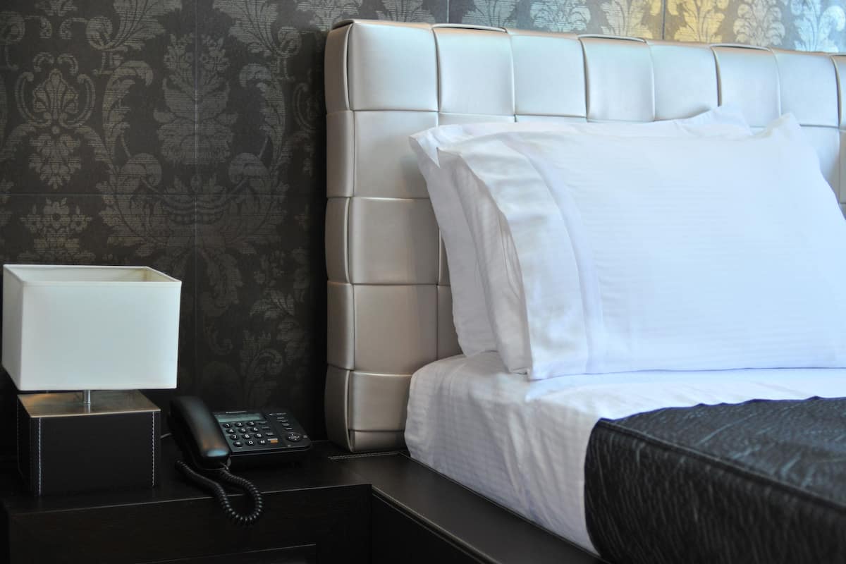 A hotel room with a tufted headboard, white bedding, a bedside telephone, and a nightstand.