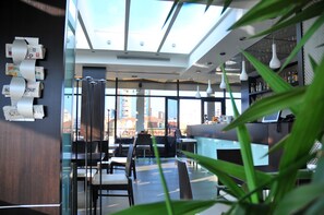A modern interior with a bar area, seating, and large windows offering a city view. - MonarC Hotel (Tirana)