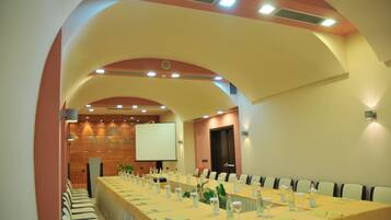 Un salón de conferencias con una larga mesa, sillas y una pantalla de proyector.