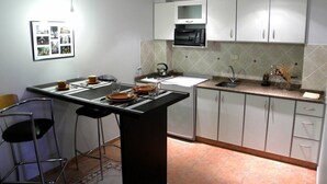 A compact kitchen with a central island, a microwave, and a sink. There are two bar stools and a framed photo on the wall. - Santiago Building (Córdoba)