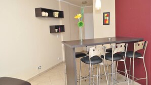A small bar area with a dark bar counter and four bar stools. There are two shelves above the counter, one with decorative items and the other with a framed picture. - Santiago Building (Córdoba)