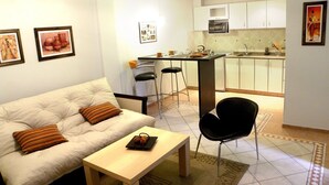 A compact living space with a sofa, a small table, a kitchen area with a bar, and a dining area with two chairs. - Santiago Building (Córdoba)