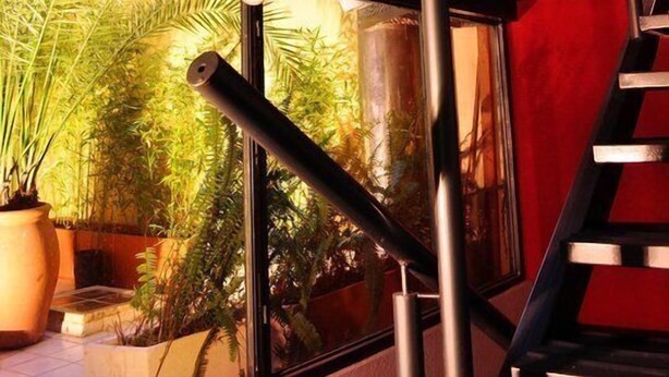 A modern staircase with glass railings, surrounded by potted plants and a view of the outside. - Santiago Building (Córdoba)