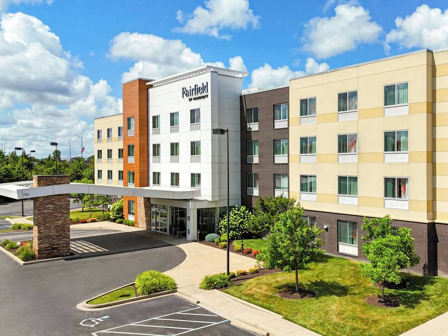 Um hotel Fairfield Inn & Suites com design moderno, apresentando entrada coberta, vários andares e estacionamento.