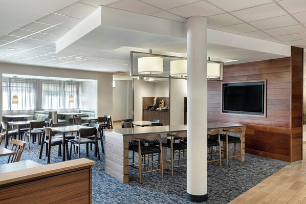 Un hall d’hôtel moderne doté d’un espace salon, d’une cuisine et d’un téléviseur fixé au mur.