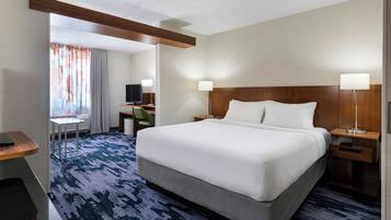 A hotel room with a large bed, a desk with a chair, a TV, and a small table.