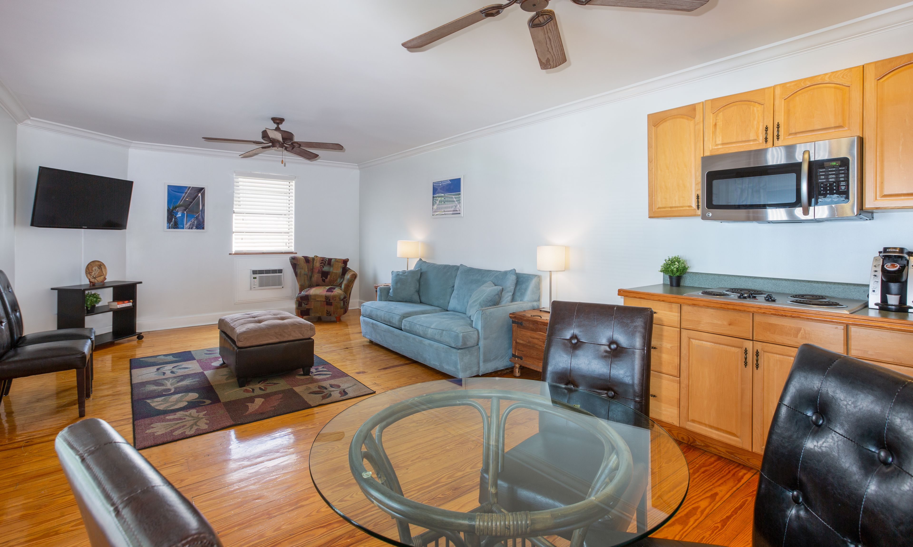A modern living room with a glass coffee table, leather armchairs, a blue sofa, and a ceiling fan.