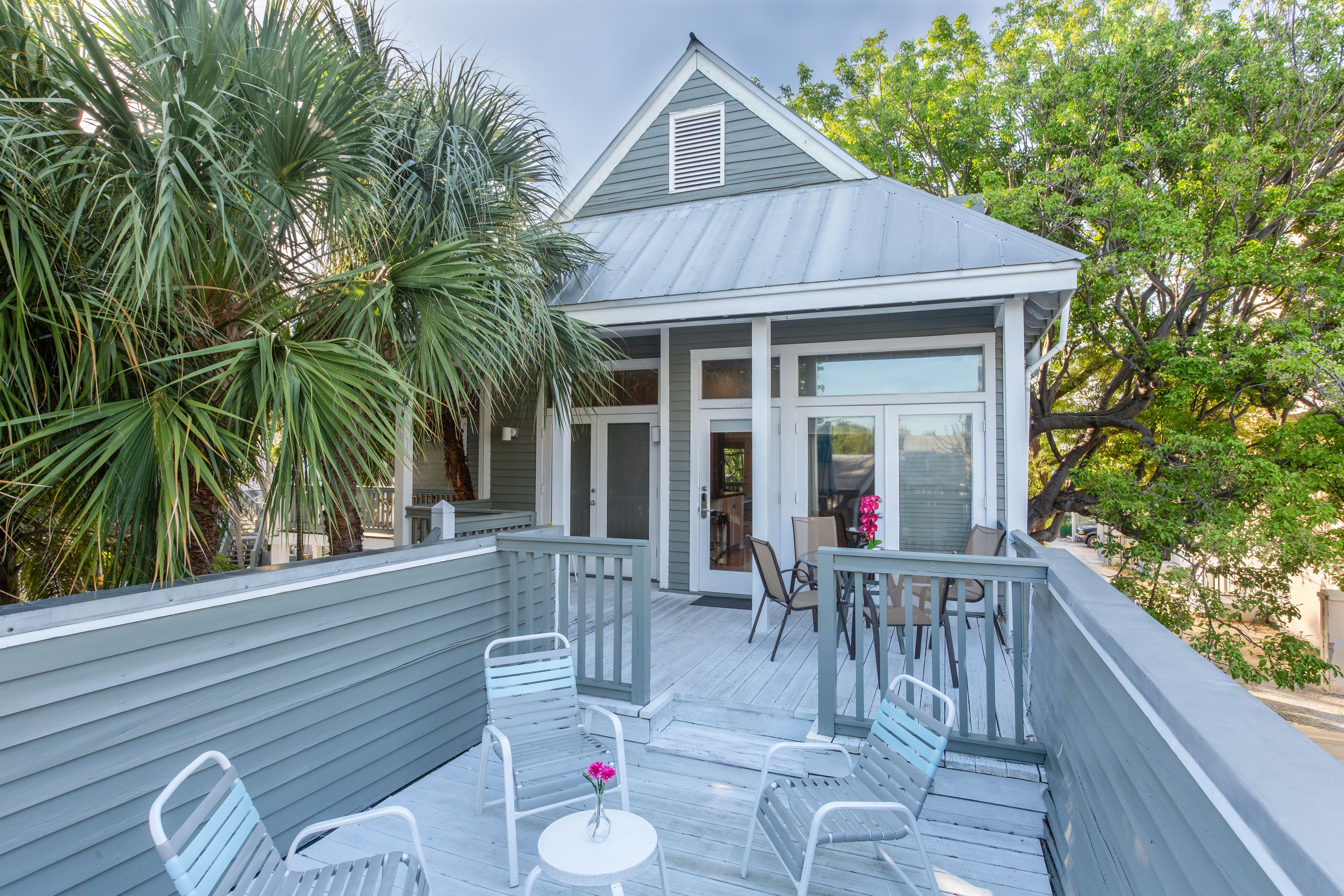 A wooden deck with outdoor seating, a small building with a porch, and surrounding greenery.