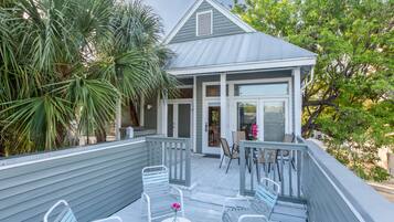 A wooden deck with outdoor seating, a small building with a porch, and surrounding greenery.