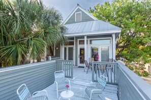 A wooden deck with outdoor seating, a small building with a porch, and surrounding greenery.