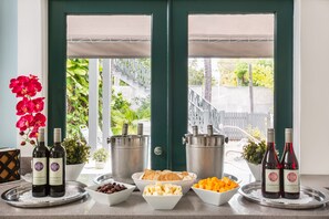 A breakfast setup with wine bottles, fruits, and pastries on a tray by a door with a view of a staircase and greenery.