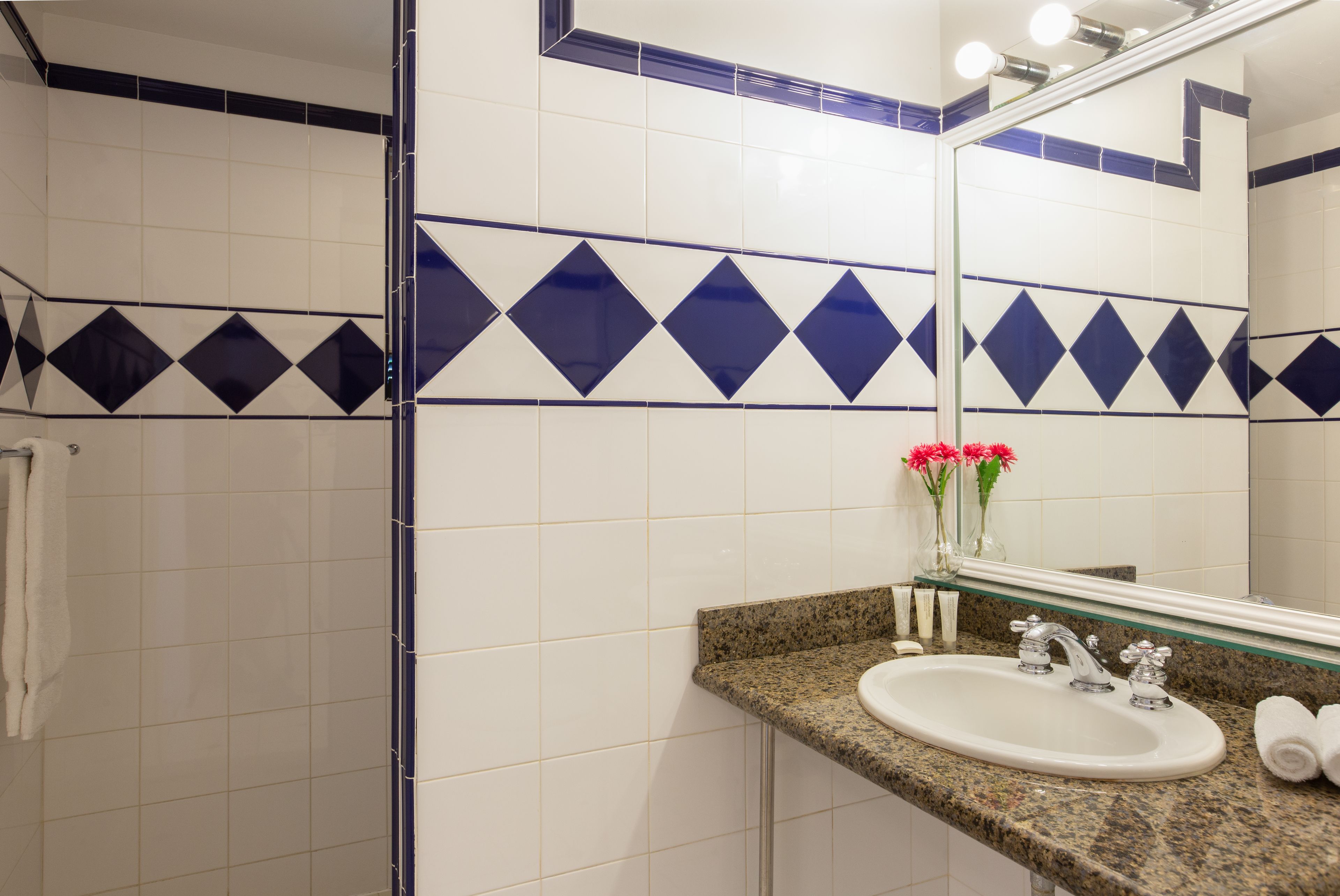 A bathroom with white tiles, a granite countertop, a sink, a mirror, and a towel rack.
