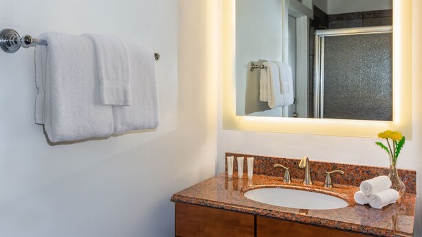 Une salle de bain avec un lavabo doté d’un plan de travail en granit, un miroir et deux serviettes suspendues à un porte-serviettes.
