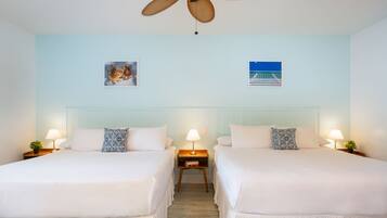 A hotel room with two beds, a ceiling fan, wall art, and bedside lamps.