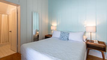 A neatly made bed with a white comforter, two bedside tables with lamps, and a door with a curtain.