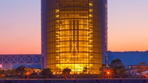 A modern cylindrical building with a glass facade, surrounded by a water body and a bridge in the background. - Hotel Kyocera (Kirishima)
