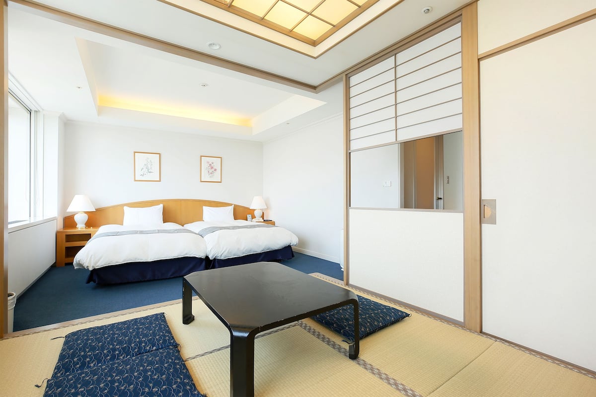 A hotel room with a bed, bedside tables, a desk, and a large window.