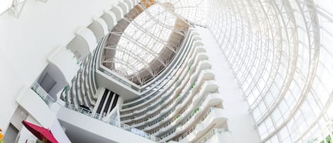 Un atrio de varios niveles con techo de vidrio, múltiples balcones y plantas de interior.